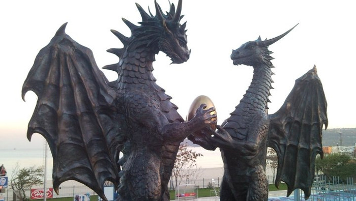 Photographie de statues de dragons à dorsales épineuses, un mâle et une femelle, face à face, qui tiennent un oeuf d’or dans leurs pattes.