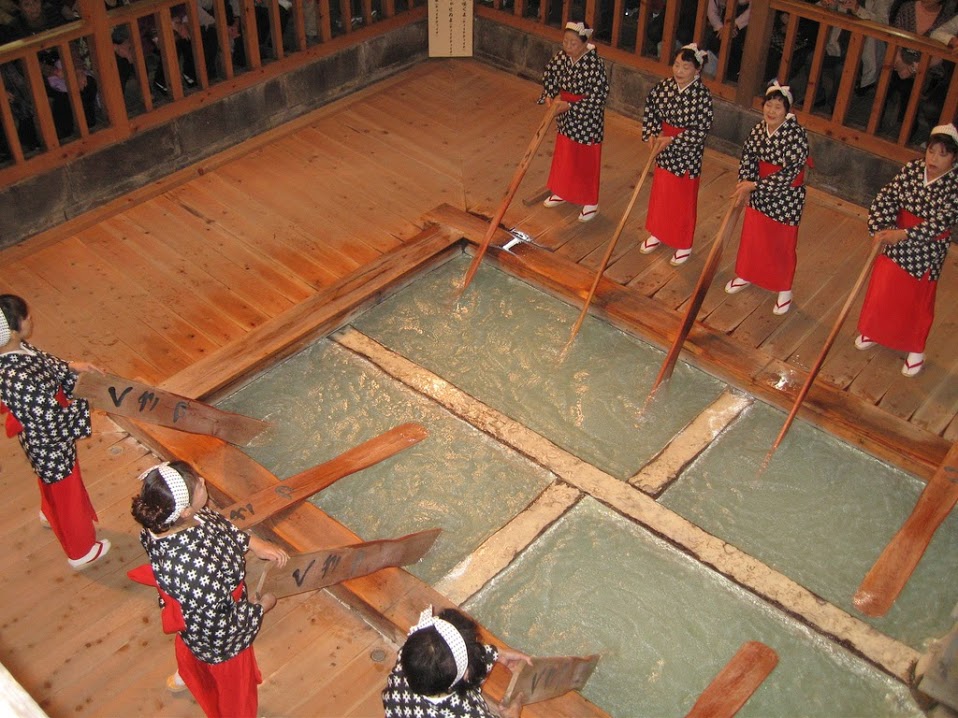 Photo de japonais en costumes traditionnels remuant l’eau des bains avec de grandes pagaies de bois