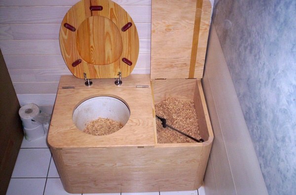 Photo de toilettes sèches d'intérieur avec bac à copeaux à côté de la cuvette.