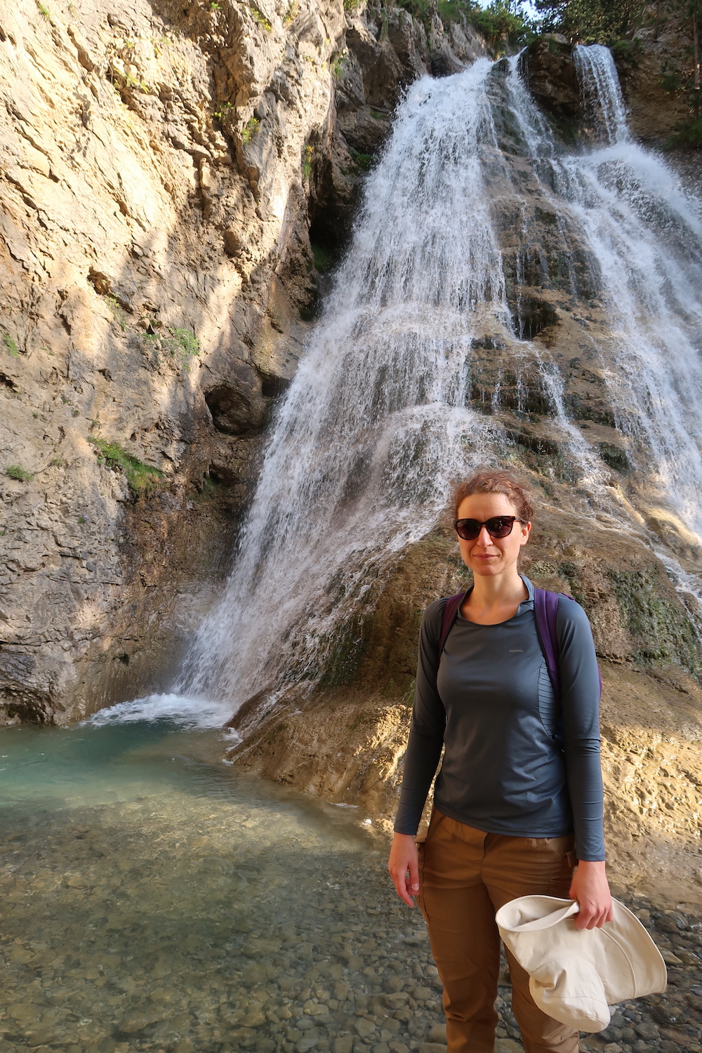 Une fille heureuse en vacances devant une cascade.