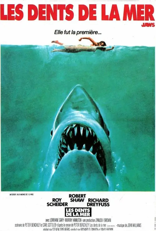 Affiche du film représentant un énorme requin dont la gueule remplie de dents monte à la surface, sous une nageuse.